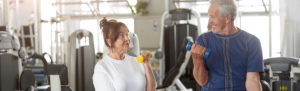 Happy senior couple training with dumbbells in gym.