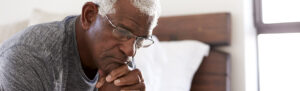 Man sitting on edge of bed looking sad