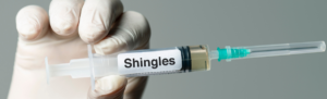 Medical gloved hand holding a syringe that says 'shingles'.