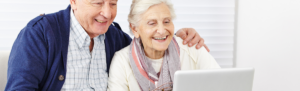 Elderly couple smiling down at a computer screen.