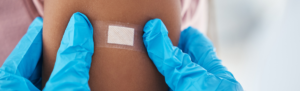 Medical gloved hands putting a bandage on a patient's arm after vaccine.