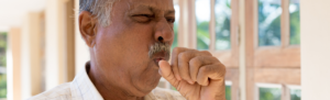 Elderly man with hand covering a cough.