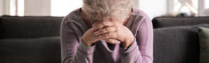 Elderly woman with her head resting in her hands.