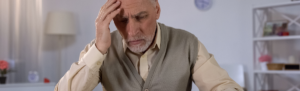 Elderly man with hand on head.
