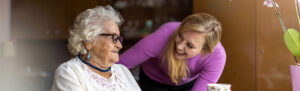 A young woman leans down to smile at an elderly woman